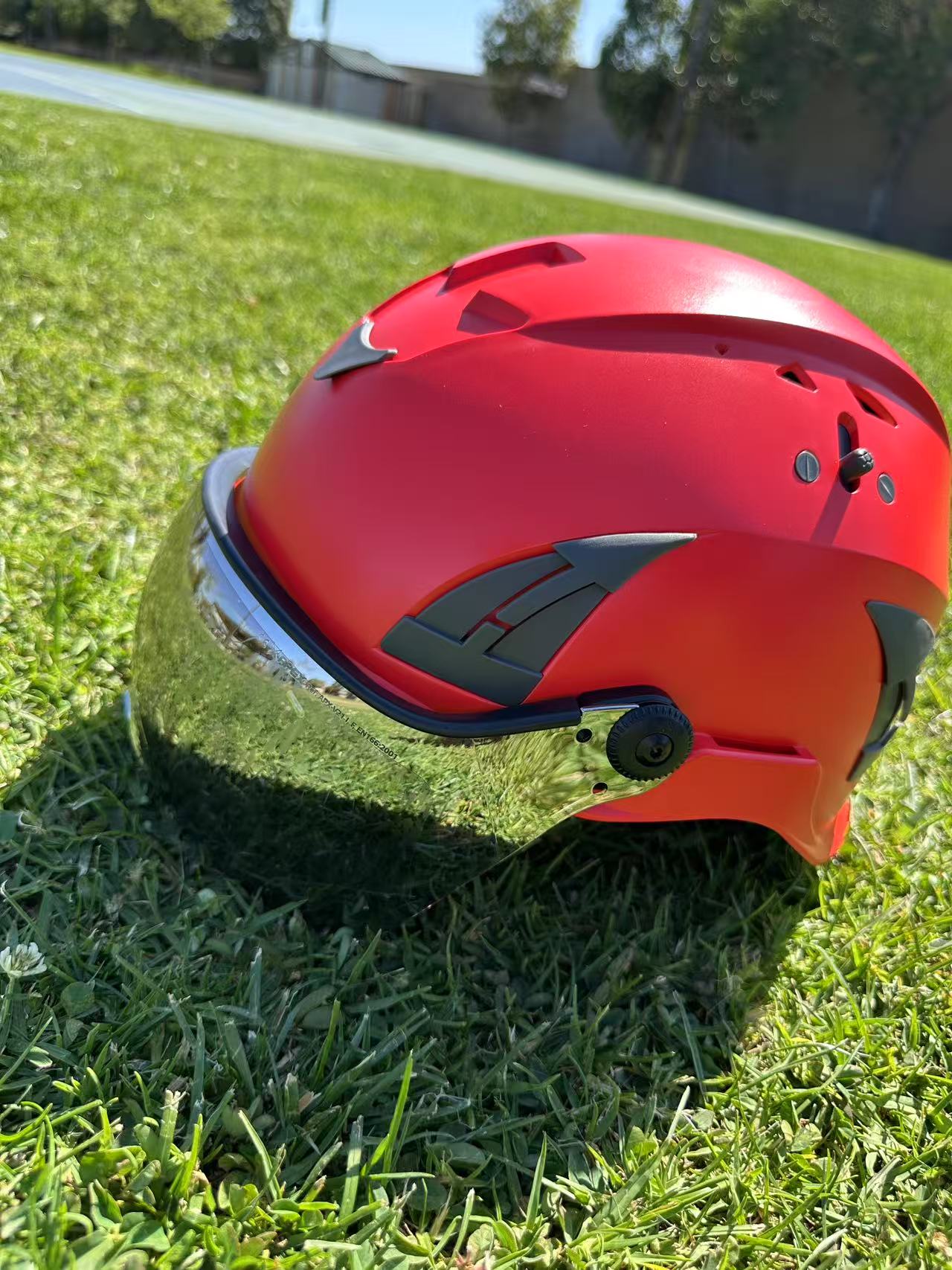 Low angle side view of AeroPro red ANSI/ISEA Z89.1-2014 Type 1 Class C Safety Helmets with Smoke Visor used for Industrial, Rescue & fall protection sitting on grass.