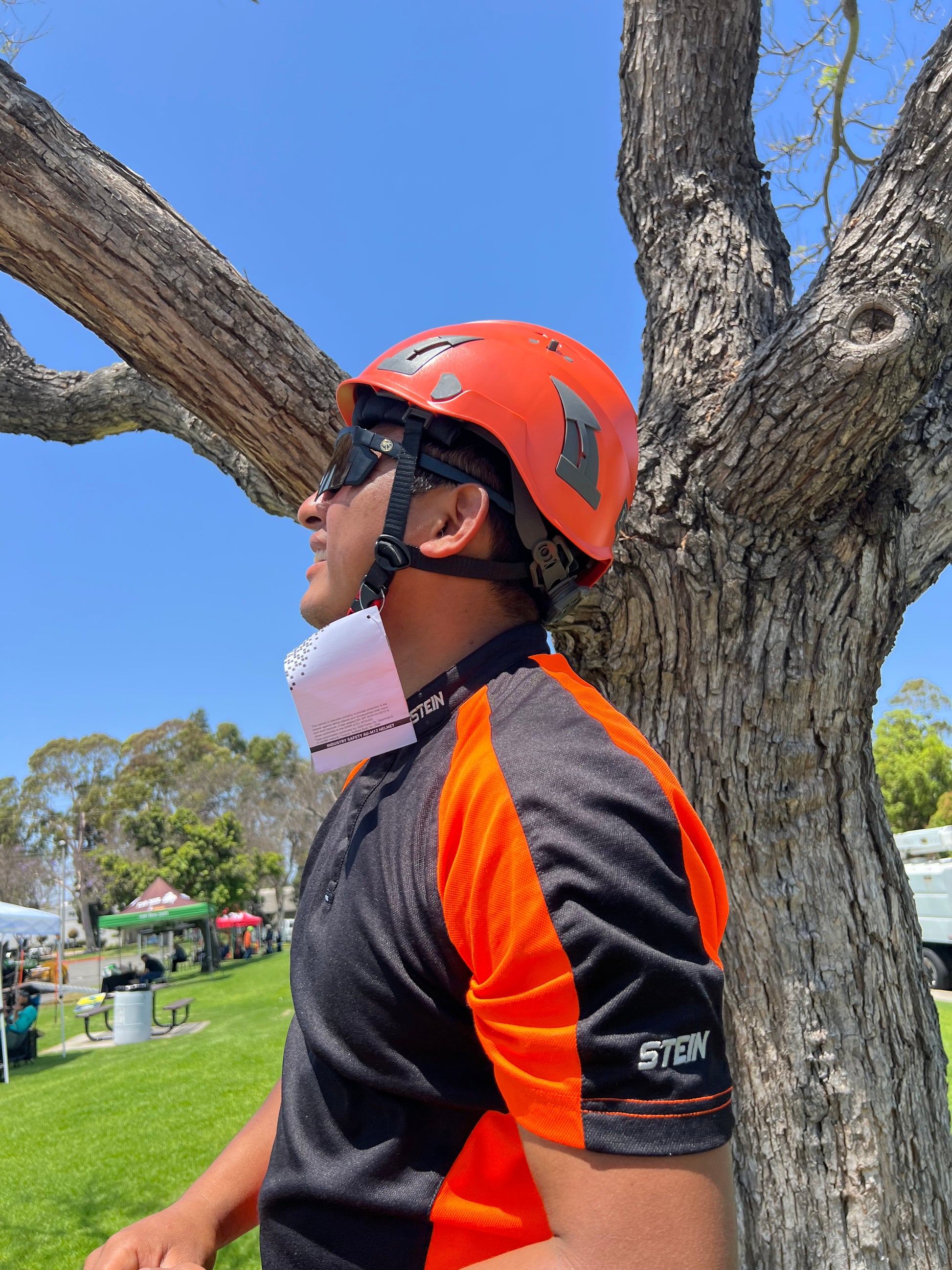 Side view of construction worker with orange  AeroPro Safety Helmet ANSI/ISEA Z89.1-2014 OSHA Certified Type 1 Class C, gearing up to climb tree.